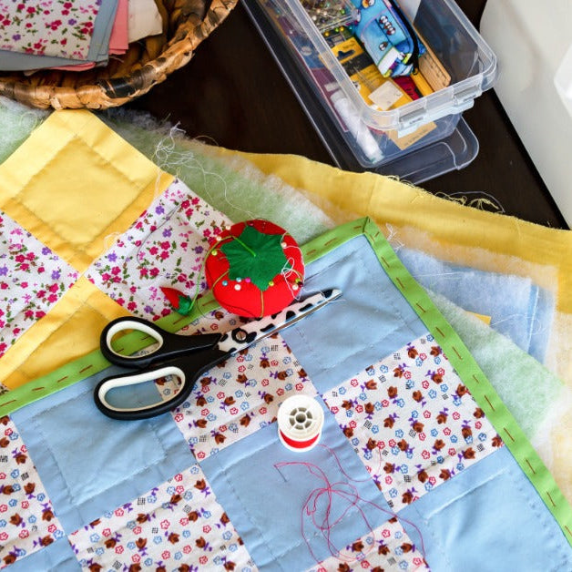 Several patchwork quilt squares, batting, scissors, a pincushion, thread, extra fabric squares, and a sewing machine on a table.