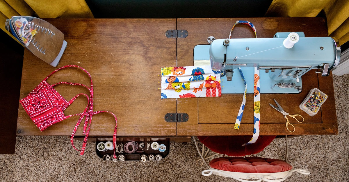 An overhead view of a wooden sewing cabinet with a sewing machine, unfinished project, and various tools on it.