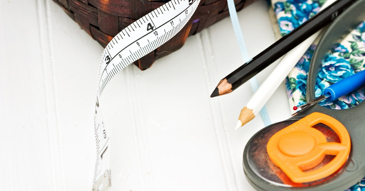 Several sewing notions, including a measuring tape, fabric pencils, and rotary cutter, against a white surface.
